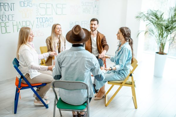 Group of diverse people keeping hands together, sitting in a circle during the psychological therapy, feeling support from each other