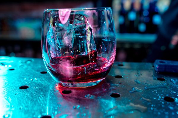Close up of alcoholic cocktail, beverage, drink, prepared by professional barman in multicolored neon light. Entertainment, drinks, service concept. Modern bar, trendy neoned colors, copyspace.