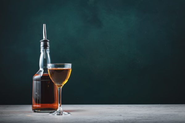 Spanish sherry brandy in glass with bottle on dark green background